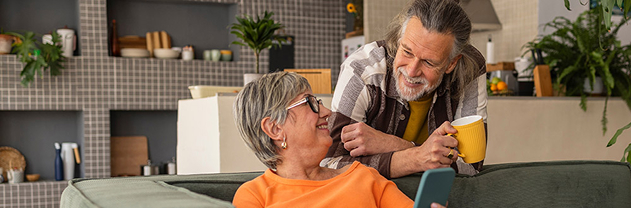 Older woman sitting on a couch smiling at an older man leaning behind her Older woman sitting on a couch smiling at an older man leaning behind her